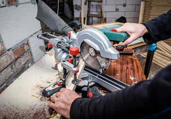 Carpenter cutting wooden plank using sliding compound mitre saw