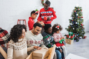 cheerful african american family packing presents in living room with blurred christmas tree