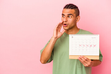 Young venezuelan man holding a calendar isolated on pink background is saying a secret hot braking news and looking aside