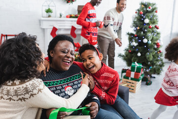 happy boy and woman embracing laughing african american granny near blurred men and christmas tree in living room - Powered by Adobe