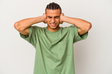 Young venezuelan man isolated on white background covering ears with hands trying not to hear too loud sound.