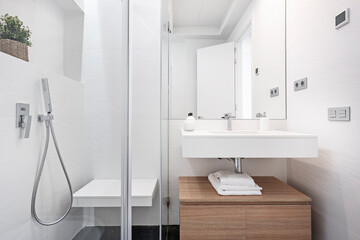 Bathroom with tiled shower in white tones with wooden cabinet and white washbasin in vacation rental apartment
