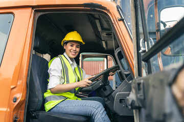 Asian woman truck driver sitting in truck cabin looking at camera.