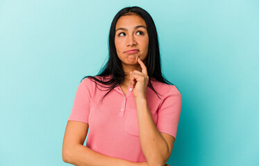 Young Venezuelan woman isolated on blue background looking sideways with doubtful and skeptical expression.