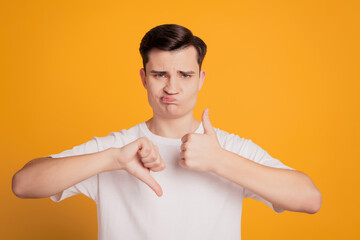 Portrait of doubtful unsure guy make choice show thumb up down on yellow background