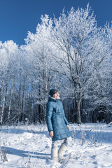 Young woman is resting in the winter forest. Blue coat on a background of white snow