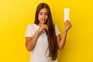 Young caucasian woman holding a compress isolated on yellow background keeping a secret or asking for silence.