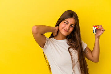 Young caucasian woman holding a home keys isolated on yellow background touching back of head, thinking and making a choice.