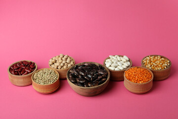 Bowls with different types of beans on pink background