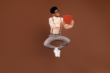 Photo of geek guy jump hold open book read interesting story wear suspenders shoes isolated brown...