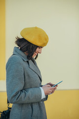 Woman using smartphone and wearing yellow beret and a gray coat