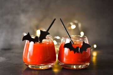 Halloween Cocktail. Food Concept. Glasses with Black Bats and light garland on a gray table....