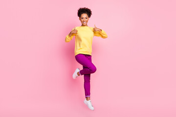Fototapeta na wymiar Photo of attractive pretty lady wear yellow pullover jumping high showing thumbs up smiling isolated pink color background