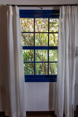 window overlooking nature on a farm in São Paulo, Brazil. Blue, old colonial windows. with white curtain