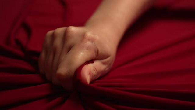 Woman hand passionately squeezes red bed sheet. Love concept.