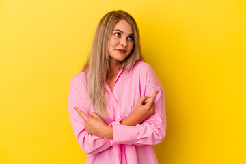 Young russian woman isolated on yellow background points sideways, is trying to choose between two options.