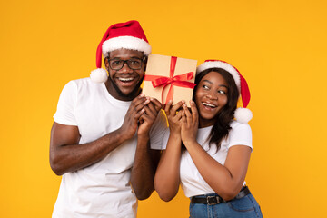 Fototapeta premium Black Couple Holding Christmas Gift Guessing What's Inside, Yellow Background