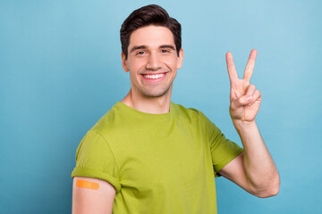 Photo of excited handsome young man guy wear green t-shirt showing sticky plaster v-sign smiling...