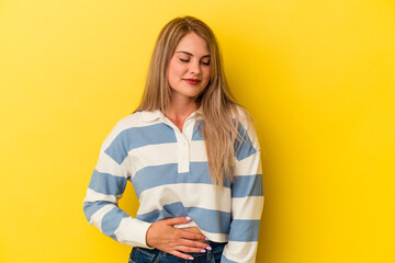Young russian woman isolated on yellow background touches tummy, smiles gently, eating and satisfaction concept.
