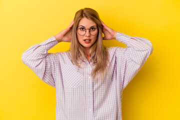 Young russian woman isolated on yellow background covering ears with hands trying not to hear too loud sound.