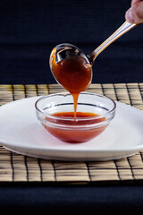 White plate with bowl of Chinese sweet and sour sauce served with ladle on black background.