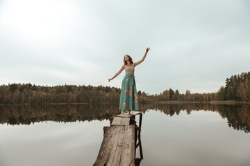 Fototapeta na wymiar A girl is dancing on a wooden bridge against the backdrop of a forest lake.