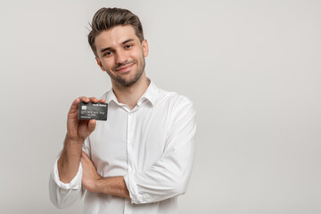 Fototapeta na wymiar Handsome man wearing white shirt showing his credit card, recommending bank, standing over white background