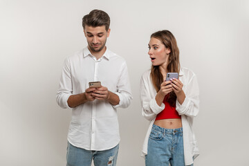 Portrait of shocked caucasian woman spying on her boyfriend using mobile phone, texting sms or scrolling social media news feed. Couple standing over white studio background