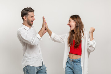 Portrait of joyful caucasian couple man and woman in casual clothes looking at each other giving high five isolated over white background