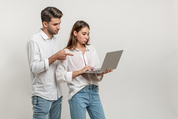 Portrait of charming inspired couple using laptop watching videos browsing sites social networks pointing on the screen isolated on white background