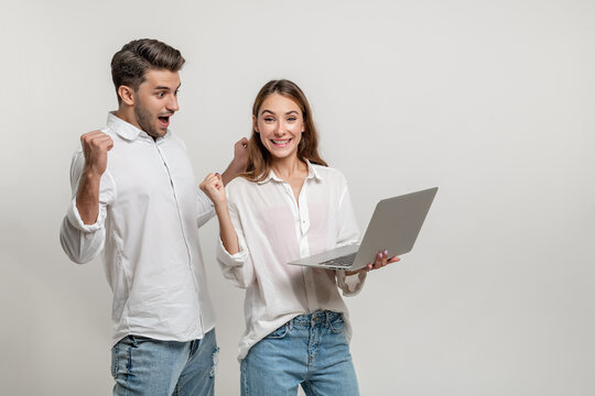 Portrait Of Excited Man And Woman Screaming And Clenching Fists Like Winners Or Happy People While Holding Laptop Isolated Over White Background