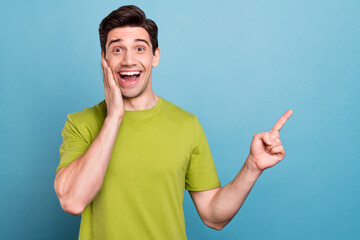Photo of sweet excited young guy dressed green t-shirt arm cheek pointing empty space smiling...