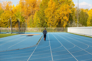 a runner trains on a running track against the background of an autumn forest