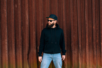 City portrait of handsome hipster guy wearing black blank hoodie with space for your logo or design. Mockup for print. Hoodie template