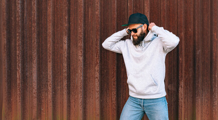 City portrait of handsome hipster guy with beard wearing gray blank hoodie with space for your logo or design. Mockup for print. Hoodie template