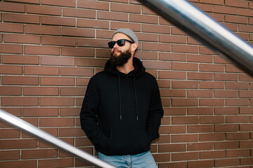 Fototapeta na wymiar City portrait of handsome hipster guy wearing black blank hoodie with space for your logo or design. Mockup for print. Hoodie template