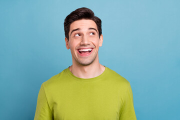 Photo of dreamy sweet young man wear green t-shirt smiling looking empty space isolated blue color background