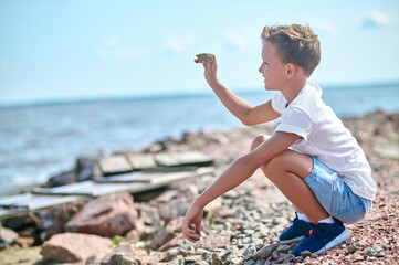 A boy in a white tshirt throwing stones to the river