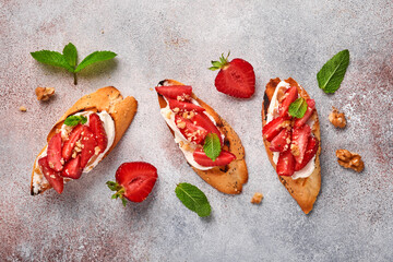 Open sandwiches with strawberries, soft cheese mint and walnut in ceramic plate on a light grey stone background. Summer and healthy dieting food, vegetarian food concept. Top view.