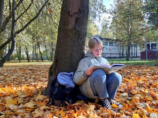 A schoolgirl is sitting by a tree reading Carol Dweck's book Flexible Consciousness.