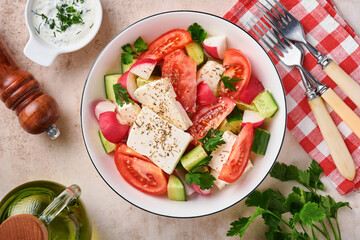 Radish, cucumber, tomato, pepper and feta cheese with spices pepper and olive oil in white bowl on grey slate, stone or concrete background. Healthy food concept. Top view.