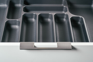 Empty open drawer of white kitchen set with black cutlery organizer tray. Storage organization system