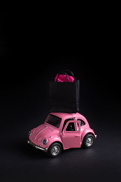 Discounts shopping, sale concept on black friday, cyber monday, pink toy car carrying a paper shopping bag on the roof on a black background.