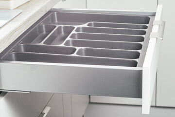 Empty open drawer of white kitchen set with black cutlery organizer tray, side view. Storage organization system