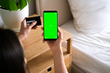 A woman makes an online order on a mobile phone with a green screen. Green screen phone background for online ordering application. Chroma key phone on credit card background