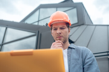 Meditative man in safety helmet looking into sketch