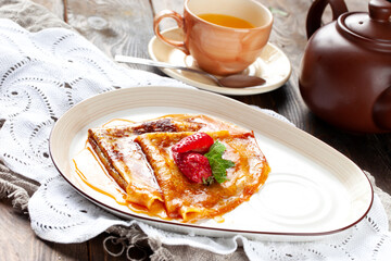 Pancakes poured with syrup and garnished with strawberries. On a wooden table.