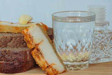 a glass of vodka next to black bread with lard and garlic
