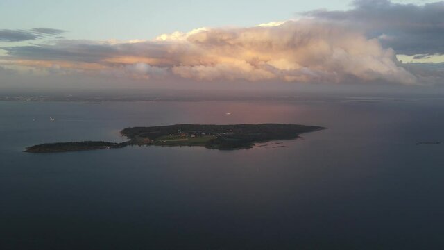 A distant drone footage of an island on sunset with colourfull couds above it. Oslofjord, Norway