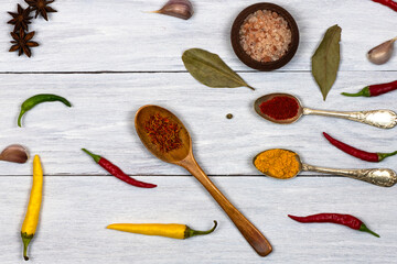 Spices, hot peppers, spoons with spices on a white wooden background.